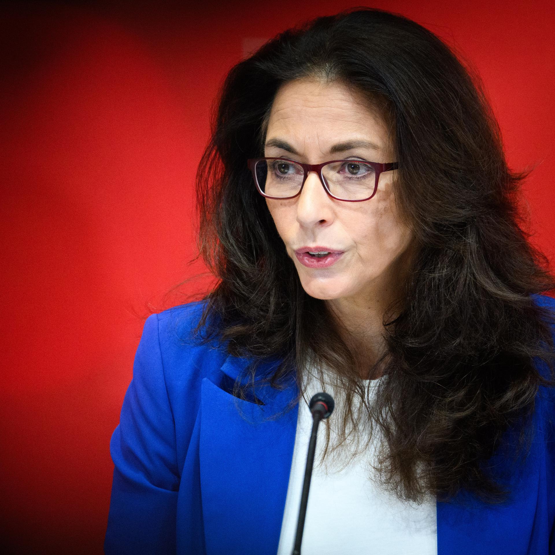 Yasmin Fahimi, Vorsitzende des Deutschen Gewerkschaftsbundes (DGB), mit Brille und dunklen langen Haaren spricht in ein Podiumsmikro vor rotem Hintergrund