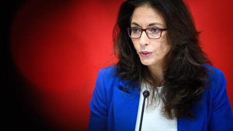 Yasmin Fahimi, Vorsitzende des Deutschen Gewerkschaftsbundes (DGB), mit Brille und dunklen langen Haaren spricht in ein Podiumsmikro vor rotem Hintergrund