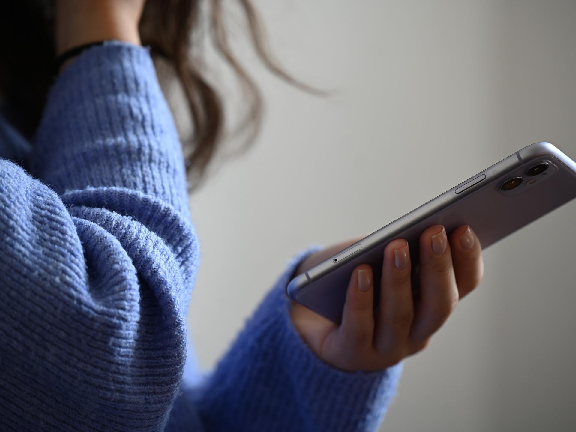 Eine Frau hält ein Smartphone in der Hand und hält sich die andere Hand offenbar vor den Mund.
