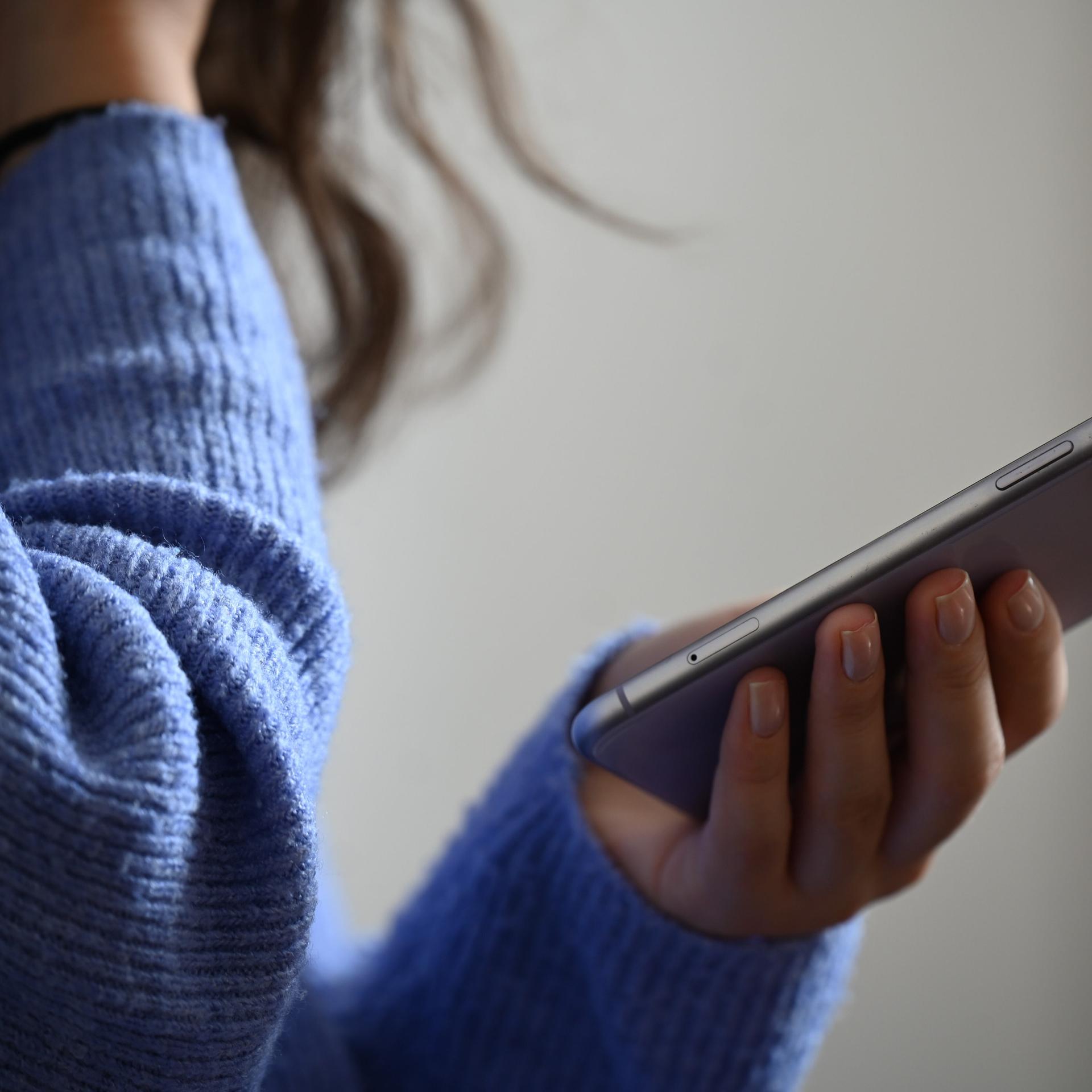 Eine Frau hält ein Smartphone in der Hand und hält sich die andere Hand offenbar vor den Mund.