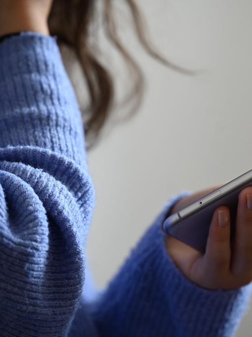 Eine Frau hält ein Smartphone in der Hand und hält sich die andere Hand offenbar vor den Mund.