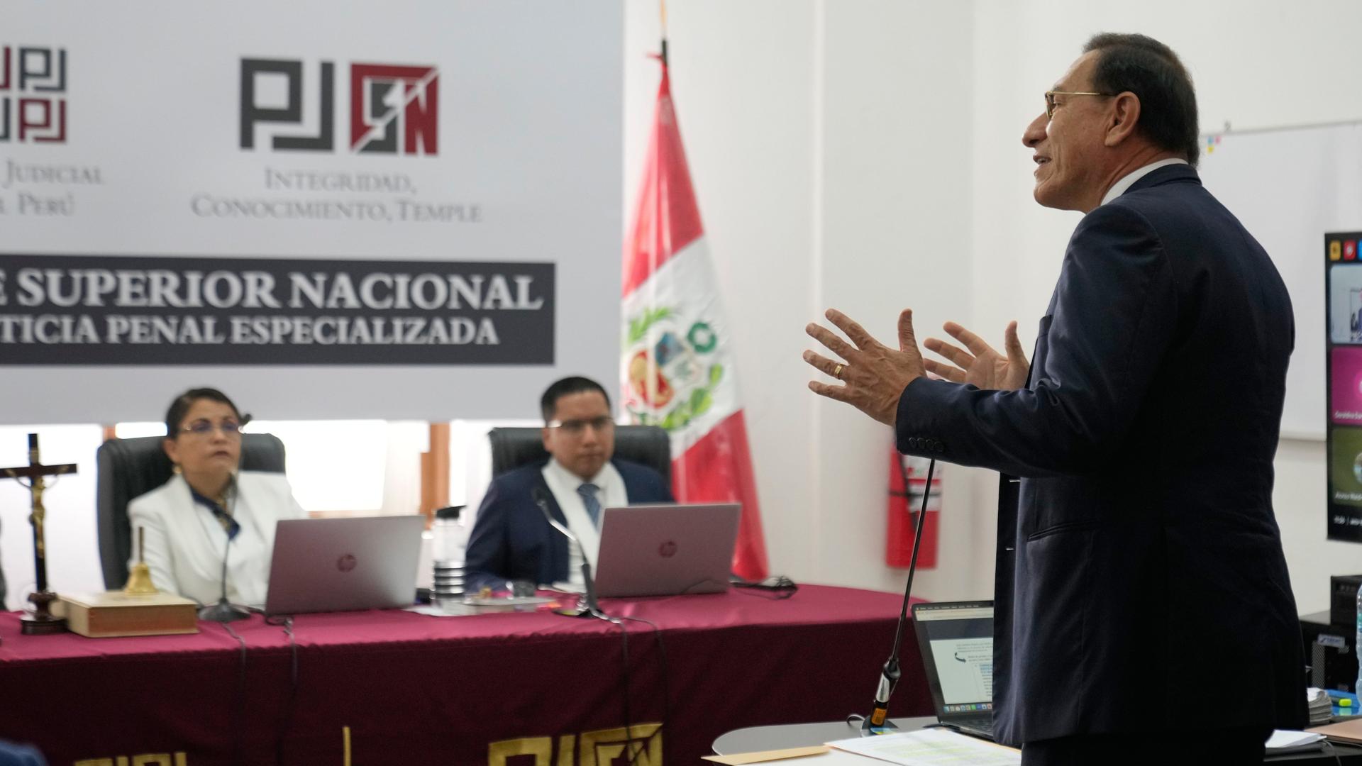 Vizcarra steht in einem Raum vor der Richterbank, sagt etwas und gestikuliert mit beiden Händen. Er trägt ein dunkles Jackett.. 