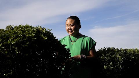 Hanya Yanagihara steht in grüner Bekleidung vor dem blauen Himmel hinter einer Hecke.