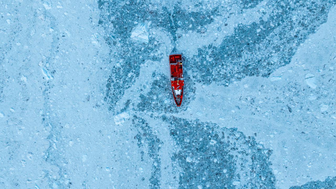 Luftaufnahme eines kleinen Schiffes, das zwischen dem Eis unterhalb des Eqi-Gletschers schwimmt, Westgrönland, Dänemark