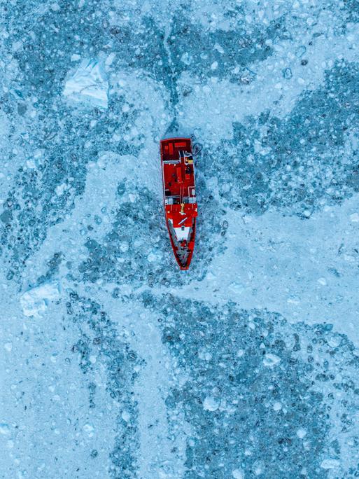 Luftaufnahme eines kleinen Schiffes, das zwischen dem Eis unterhalb des Eqi-Gletschers schwimmt, Westgrönland, Dänemark