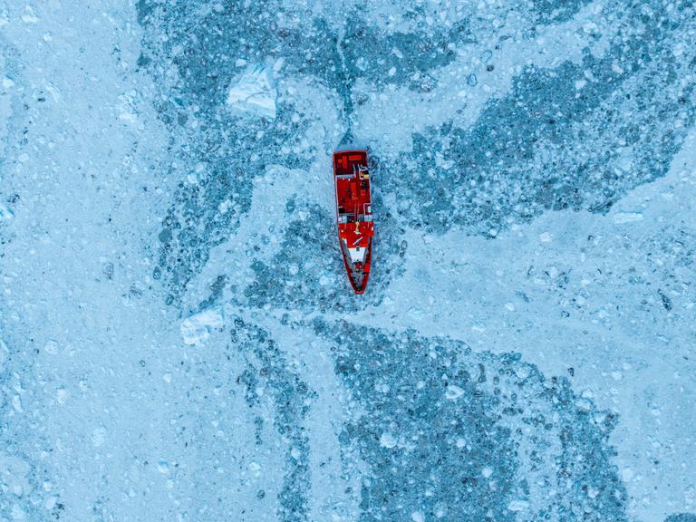 Luftaufnahme eines kleinen Schiffes, das zwischen dem Eis unterhalb des Eqi-Gletschers schwimmt, Westgrönland, Dänemark