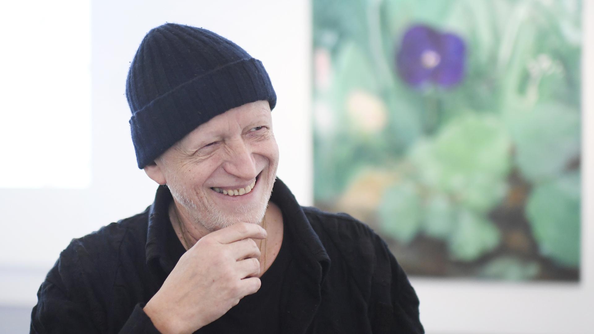 Herbert Brandl steht vor einem Gemälde und lächelt.