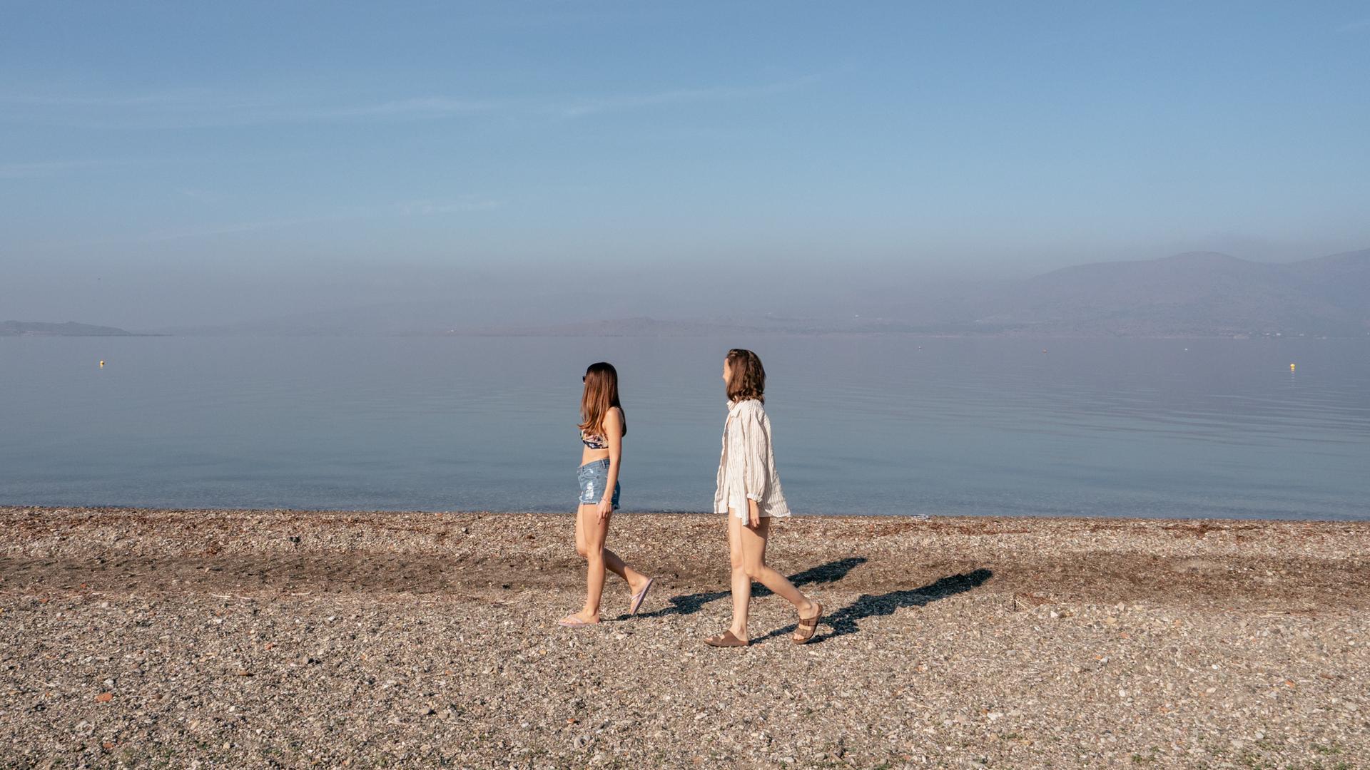 Zwei junge Frauen laufen an einem leeren Strand der griechischen Insel Lesbos Zwei junge Frauen laufen an einem leeren Strand der griechischen Insel Lesbos