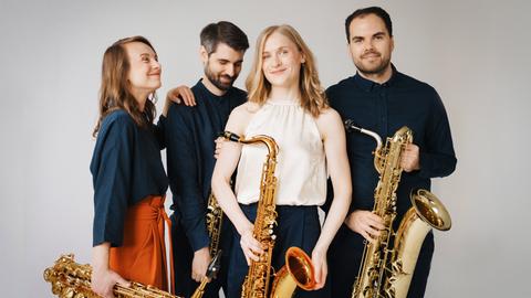 Die vier Musikerinnen und Musiker stehen in Freizeitkleidung locker beieinander, jeder hat sein Instrument bei sich.