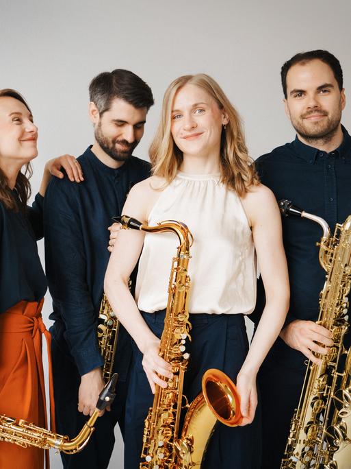 Die vier Musikerinnen und Musiker stehen in Freizeitkleidung locker beieinander, jeder hat sein Instrument bei sich.