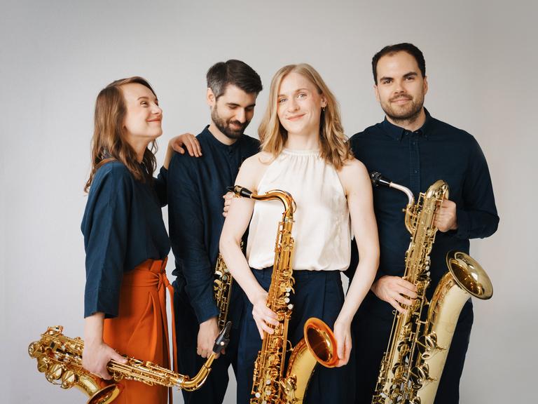 Die vier Musikerinnen und Musiker stehen in Freizeitkleidung locker beieinander, jeder hat sein Instrument bei sich.