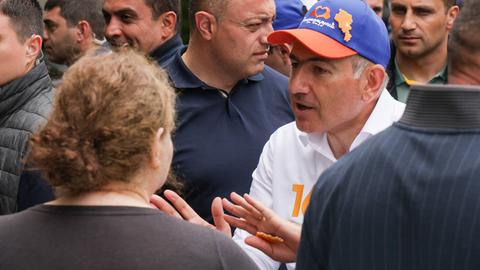Nikol Paschinjan steht in einer Menschenmenge und spricht gestikulierend. Er trägt eine blaue-orangene Basecap.