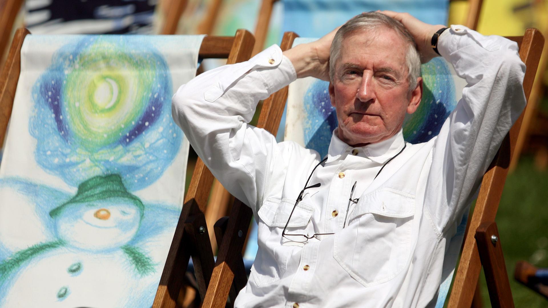 Raymond Briggs sitzt in einem Liegestuhl, daneben eine seiner Illustrationen des "Snowman"