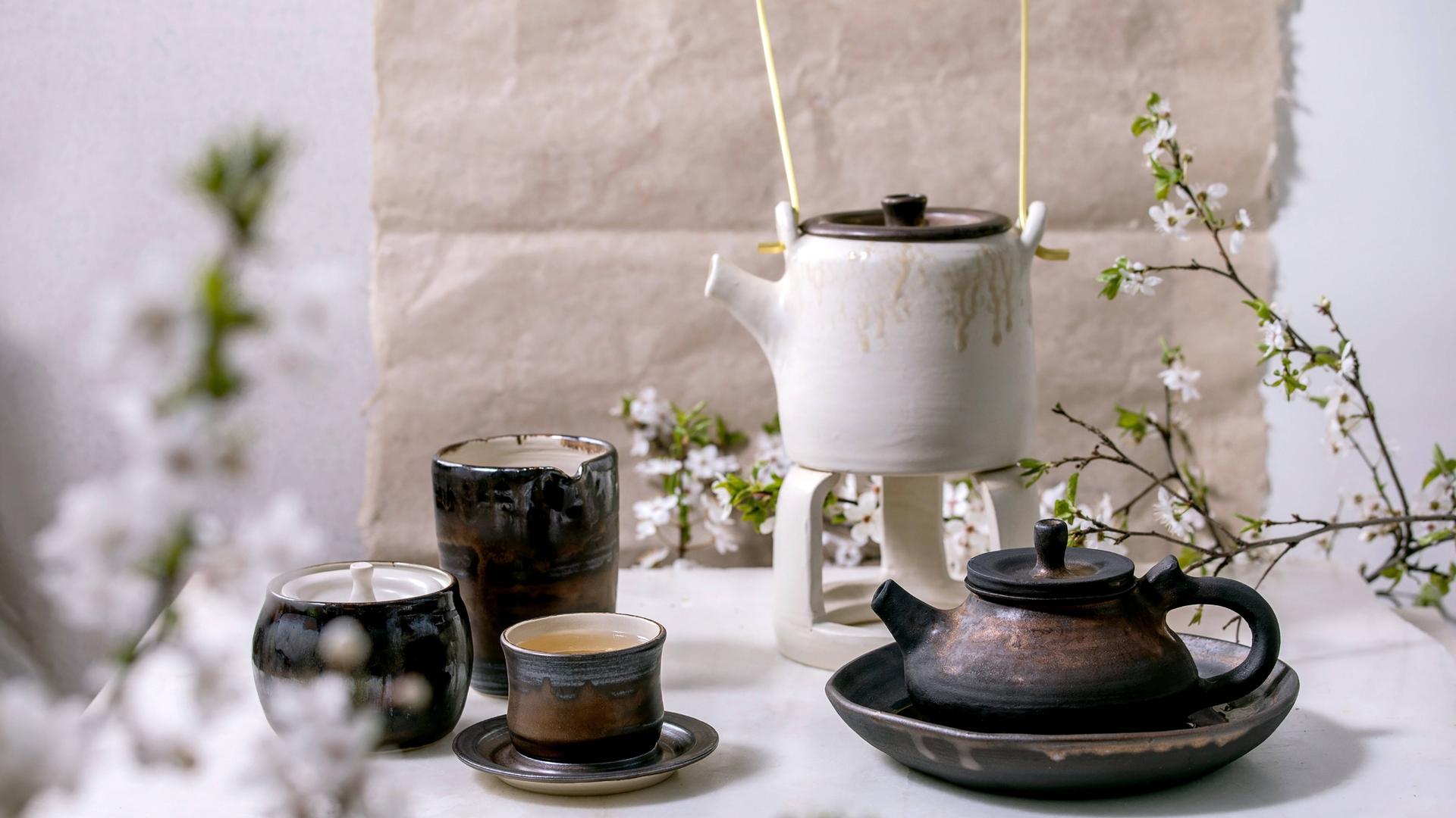 Teetassen und Kannen aus Keramik neben Zweigen eines Kirschbaums
