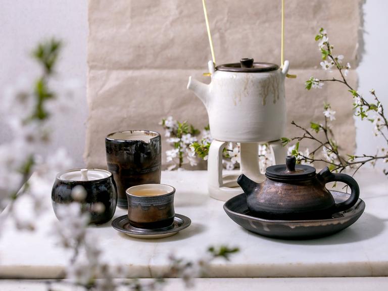 Teetassen und Kannen aus Keramik neben Zweigen eines Kirschbaums