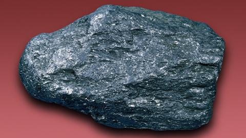 Ein dunkles Graphit-Mineral aus Sri Lanka ist vor einem roten Hintergrund zu sehen.