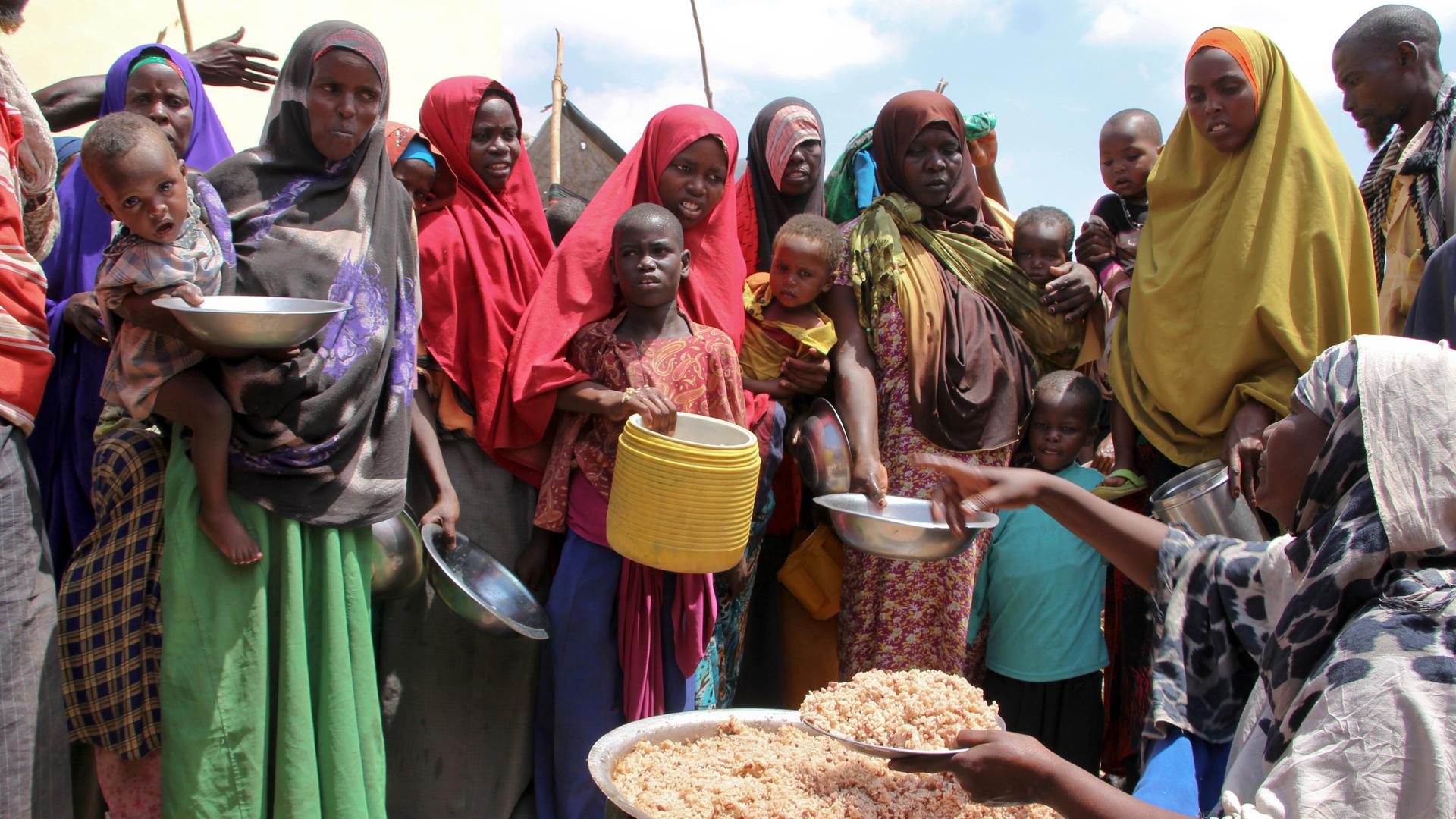 (Archiv) Frauen und Kinder stehen in Somalia mit Gefäßen in den Händen um eine Person herum, die Lebensmittel verteilt.