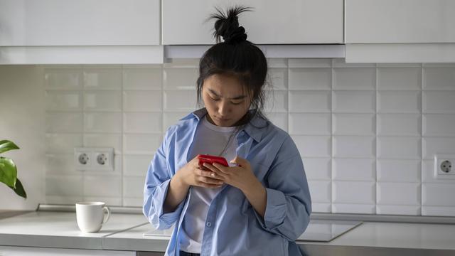 Das Foto zeigt eine junge Frau, die nachdenklich auf ihr Handy schaut. 