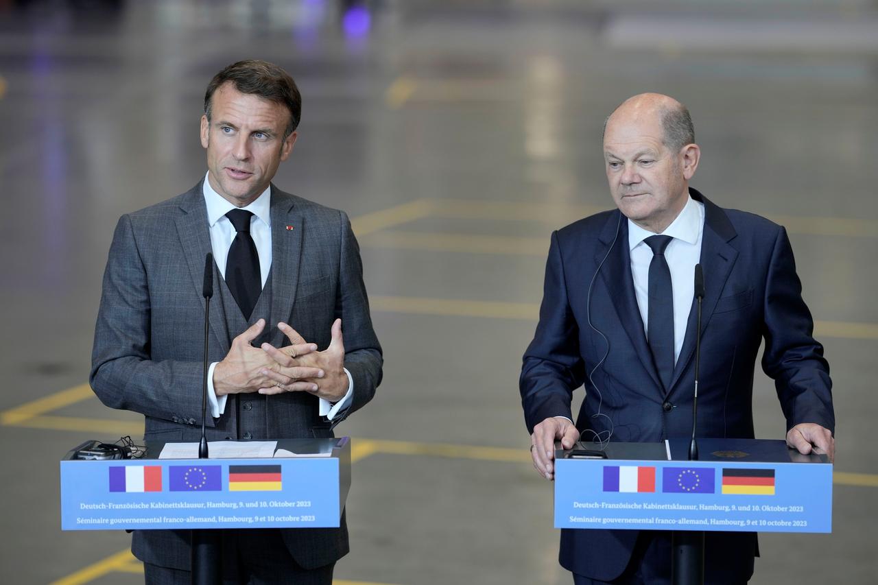 Der französische Präsident Macron und Bundeskanzler Kohl stehen jeweils an Pulten mit Mikrofonen. Vorn an den Pulten sind die Fahnen von Frankreich, der EU und Deutschland zu sehen. 