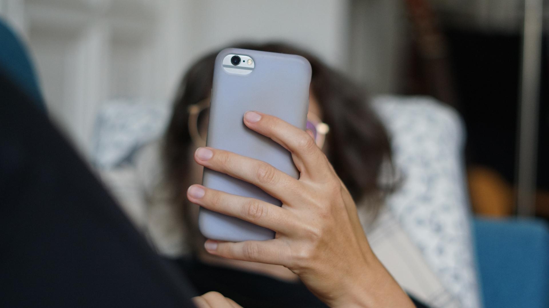 Eine Frau liegt auf einem Sofa und schaut auf ihr Smartphone 
