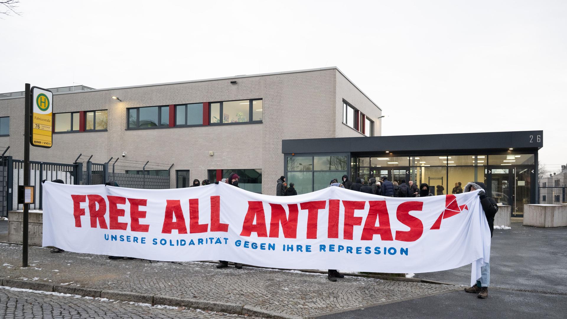 Teilnehmer einer Kundgebung stehen vor dem Oberlandesgericht Dresden (OLG) und halten ein Transparent mit der Aufschrift "Free All Antifas". 