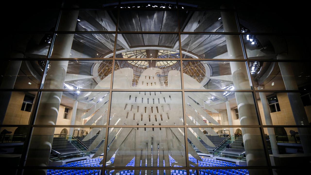 Deutscher Bundestag mit Bundesadler im Vordergrund an einer Fensterscheibe.