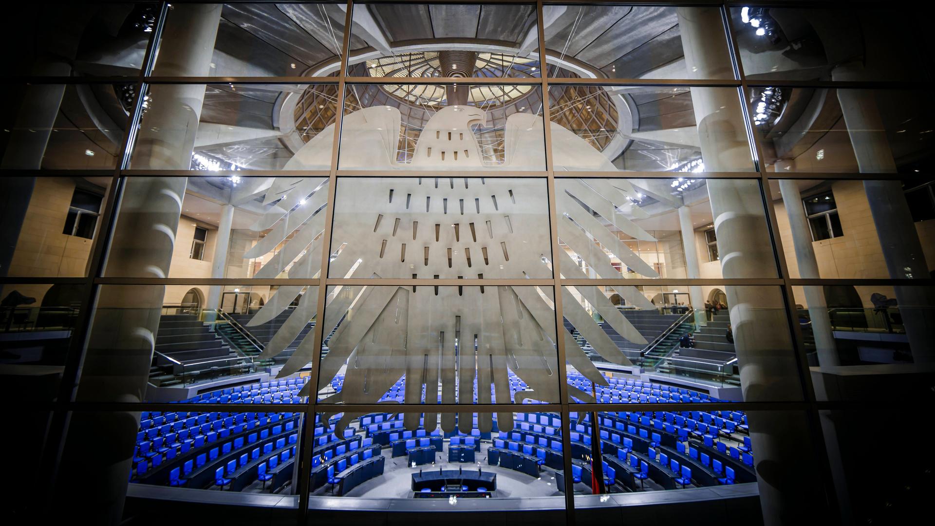 Deutscher Bundestag mit Bundesadler im Vordergrund an einer Fensterscheibe.