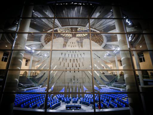 Deutscher Bundestag mit Bundesadler im Vordergrund an einer Fensterscheibe.