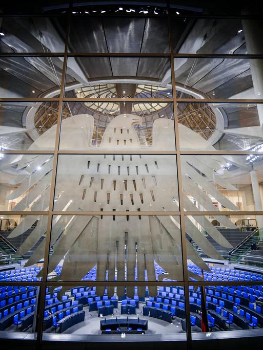 Deutscher Bundestag mit Bundesadler im Vordergrund an einer Fensterscheibe.