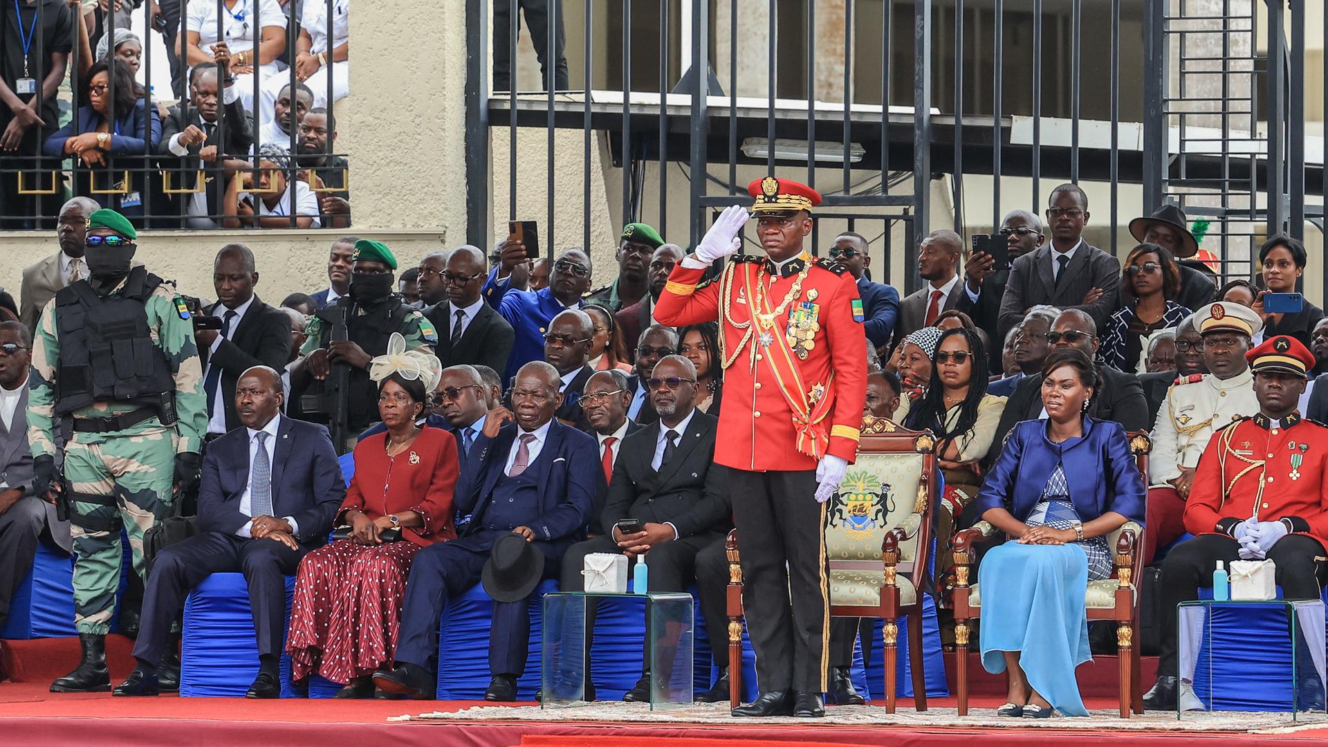 Zu sehen ist Gabuns Militärmachthaber General Brice Oligui Nguema in roter Uniform, der während einer Parade salutiert.