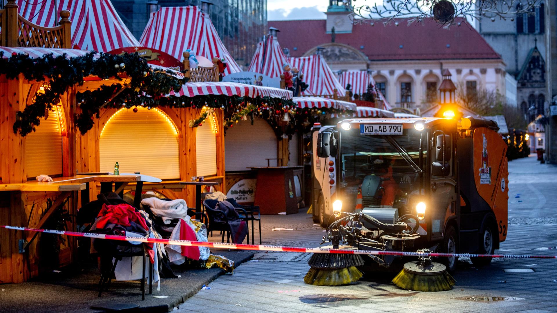 Der Magdeburger Weihnachtsmakrt mit geschlossenen Ständen. Ein Reingungsfahrzeug putzt davor die Straße. Im Hintergrund zeichnen sich Teile der Johanniskirche ab.