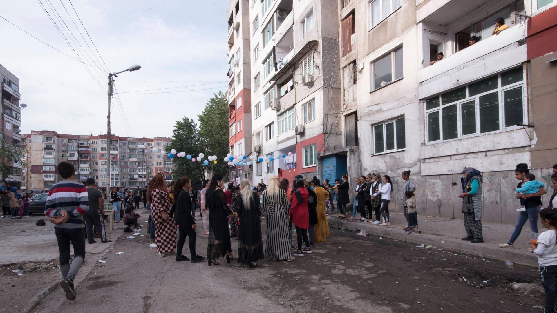 In Stolipinovo, einem Roma-Distrikt, in der bulgarischen Stadt Plovdiv feiern Menschen auf der Straße vor Plattenbauten. Die Straße ist in einem schlechten Zustand.