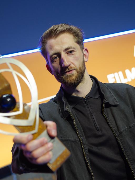 Ben Voit hält einen Pokal in die Kamera, im Hintergrund ist zu lesen: "47. Filmfestival"