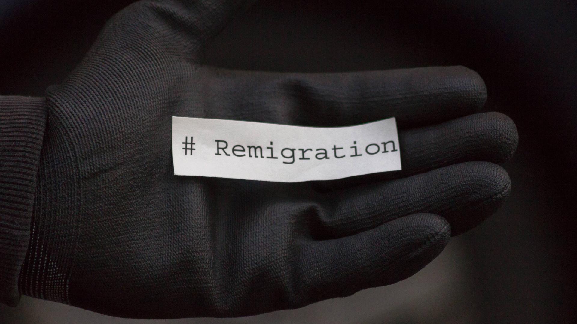 Ein schwarzer Handschuh auf dem sich ein Zettel mit der Aufschrift Remigration befindet.