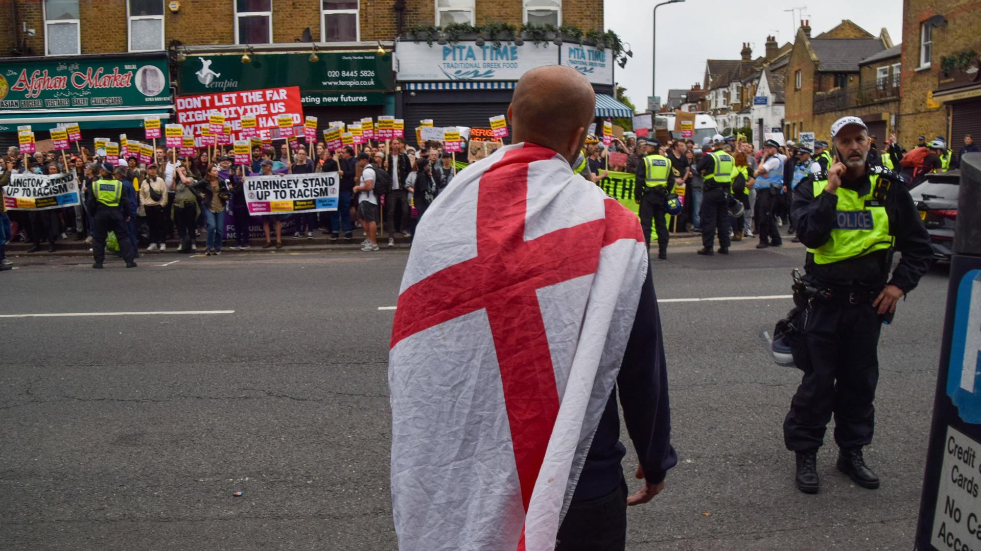 Am 7. August 2024 steht ein einzelner rechter Aktivist vor einer Menge, die gegen die rechten Ausschreitungen in Großbritannien protestiert. Dazwischen Polizisten mit gelben Westen.