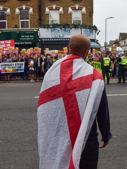 Am 7. August 2024 steht ein einzelner rechter Aktivist vor einer Menge, die gegen die rechten Ausschreitungen in Großbritannien protestiert. Dazwischen Polizisten mit gelben Westen.