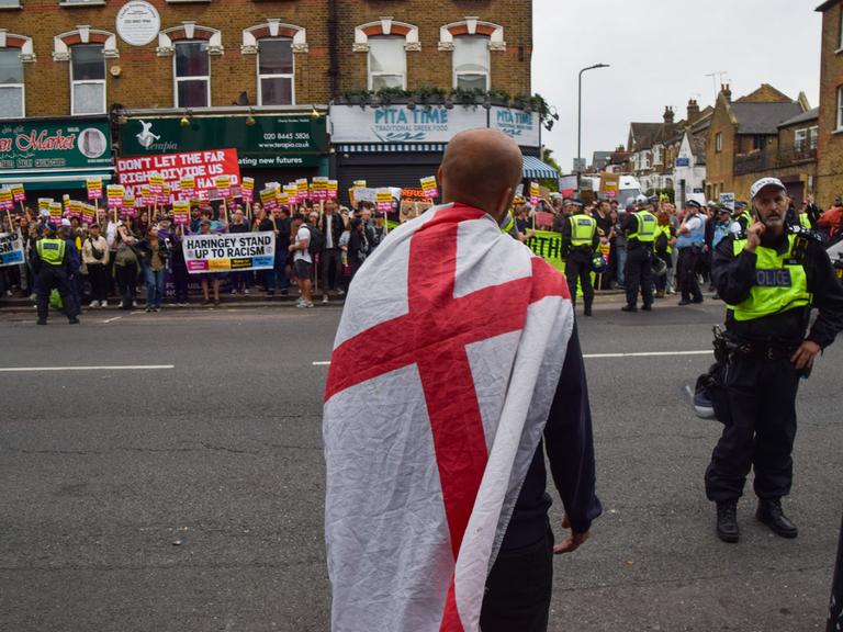 Am 7. August 2024 steht ein einzelner rechter Aktivist vor einer Menge, die gegen die rechten Ausschreitungen in Großbritannien protestiert. Dazwischen Polizisten mit gelben Westen.