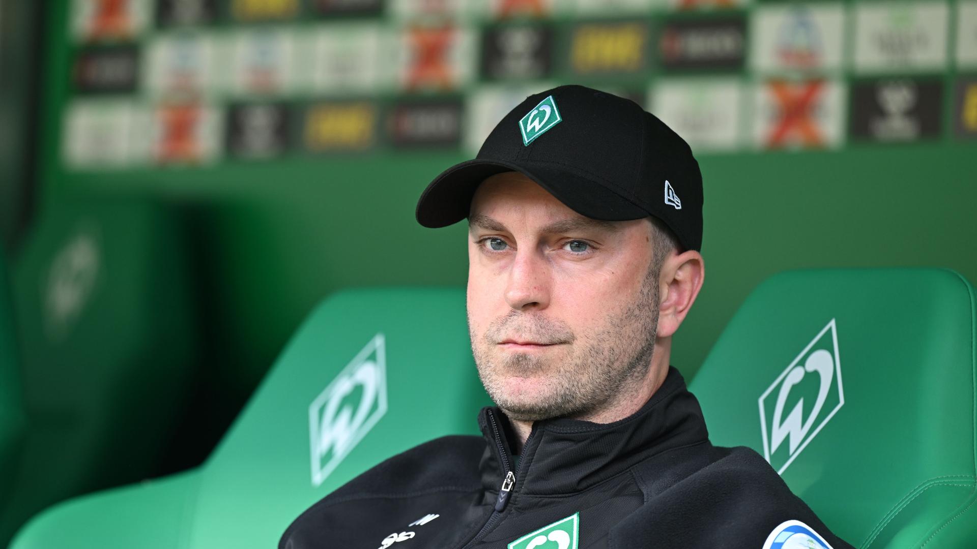 Werder-Trainer Ole Werner sitzt vor dem Spiel auf der Bank im Weserstadion und schaut ernst. 