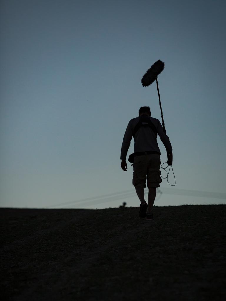 Ein Toningenieur einer Dokumentarfilmcrew geht eine Straße entlang, während im Hintergrund der Himmel dunkler wird.