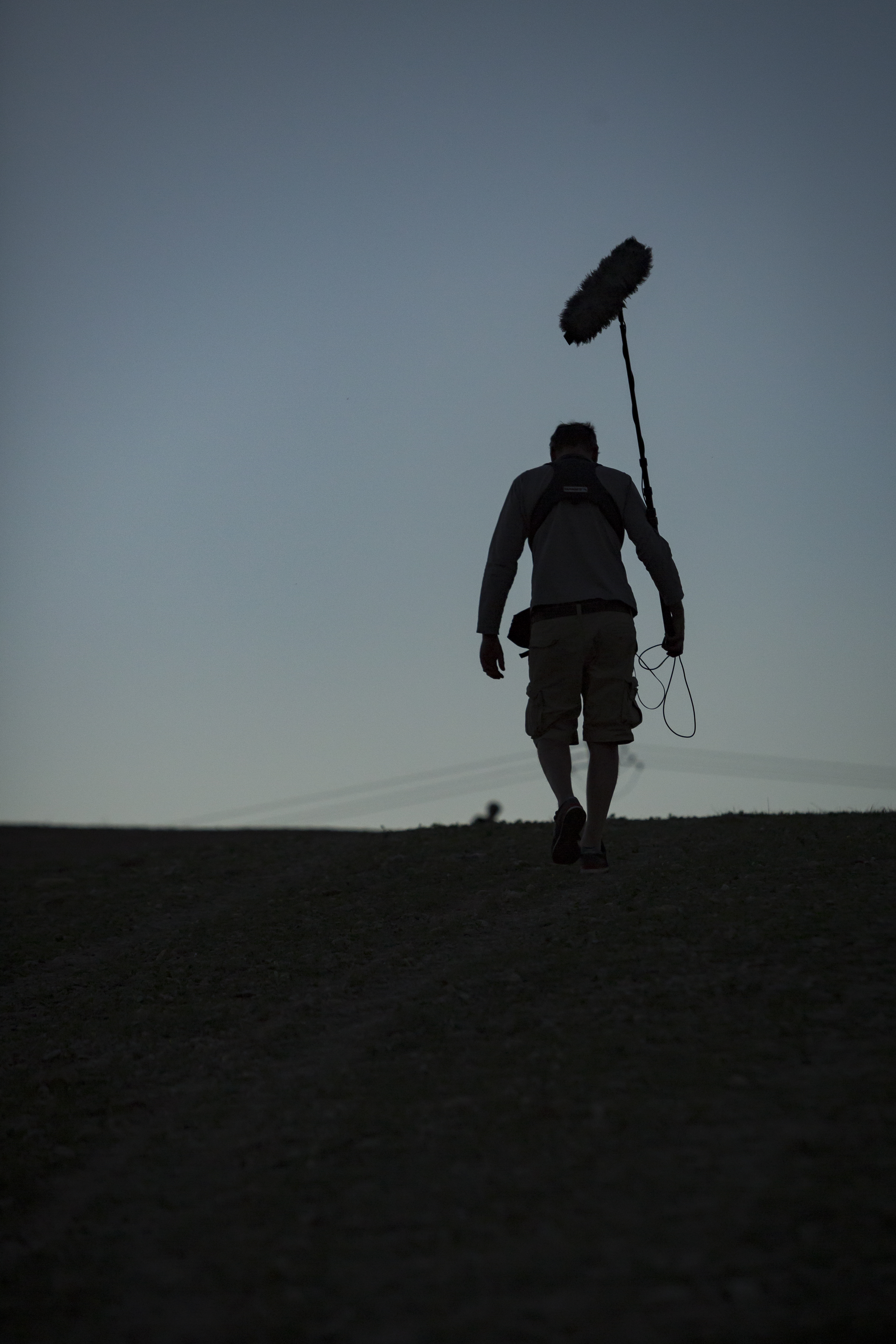 Ein Toningenieur einer Dokumentarfilmcrew geht eine Straße entlang, während im Hintergrund der Himmel dunkler wird.