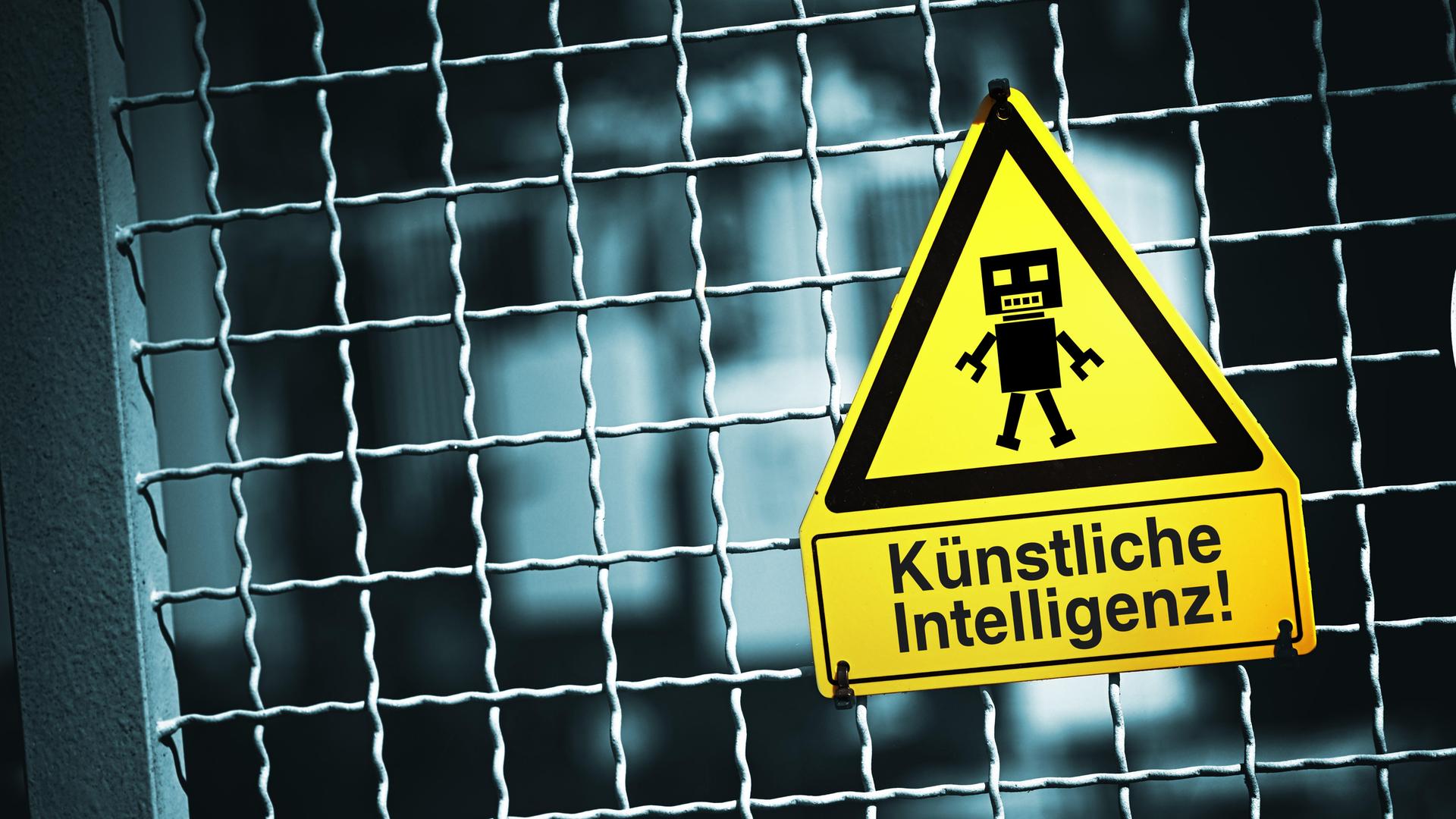 Roboterfigur auf einem Warnschild mit Aufschrift Künstliche Intelligenz (Symbolbild)
