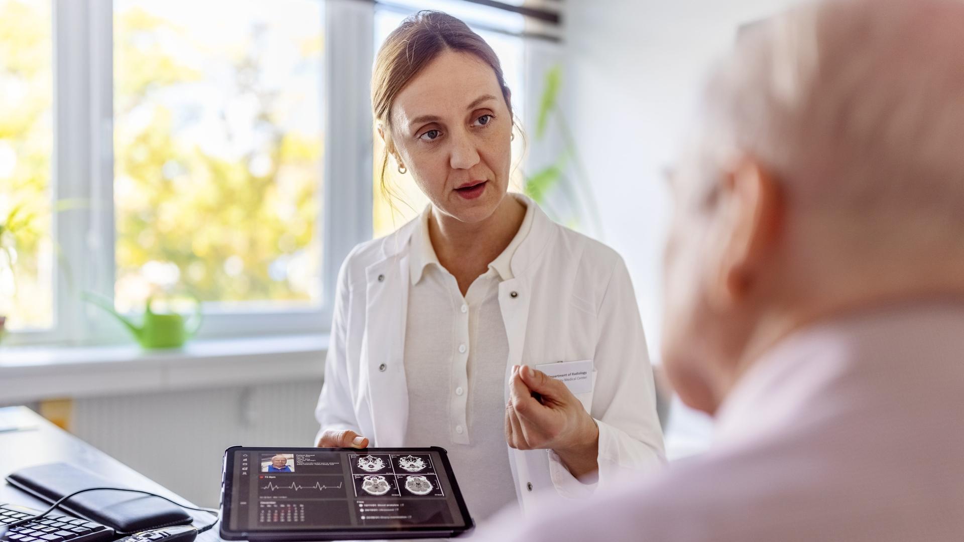 Eine Ärztin hält ein Tablet mit einem Röntgenbild und erklärt einem Patienten etwas daran.