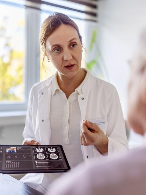 Eine Ärztin hält ein Tablet mit einem Röntgenbild und erklärt einem Patienten etwas daran.