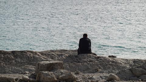 Ein Mann sitzt allein am Seeufer
