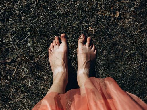 Blick auf nackte Frauenfüße im Gras, dunkel gehaltenes Bild.