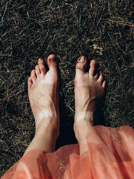 Blick auf nackte Frauenfüße im Gras, dunkel gehaltenes Bild.