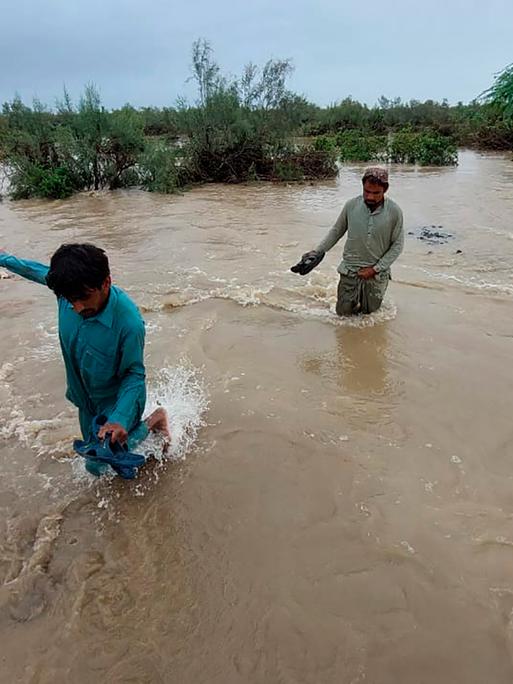 Dorfbewohner gehen durch die Fluten, die nach dem Monsunregen in Pakistan entstanden sind. 