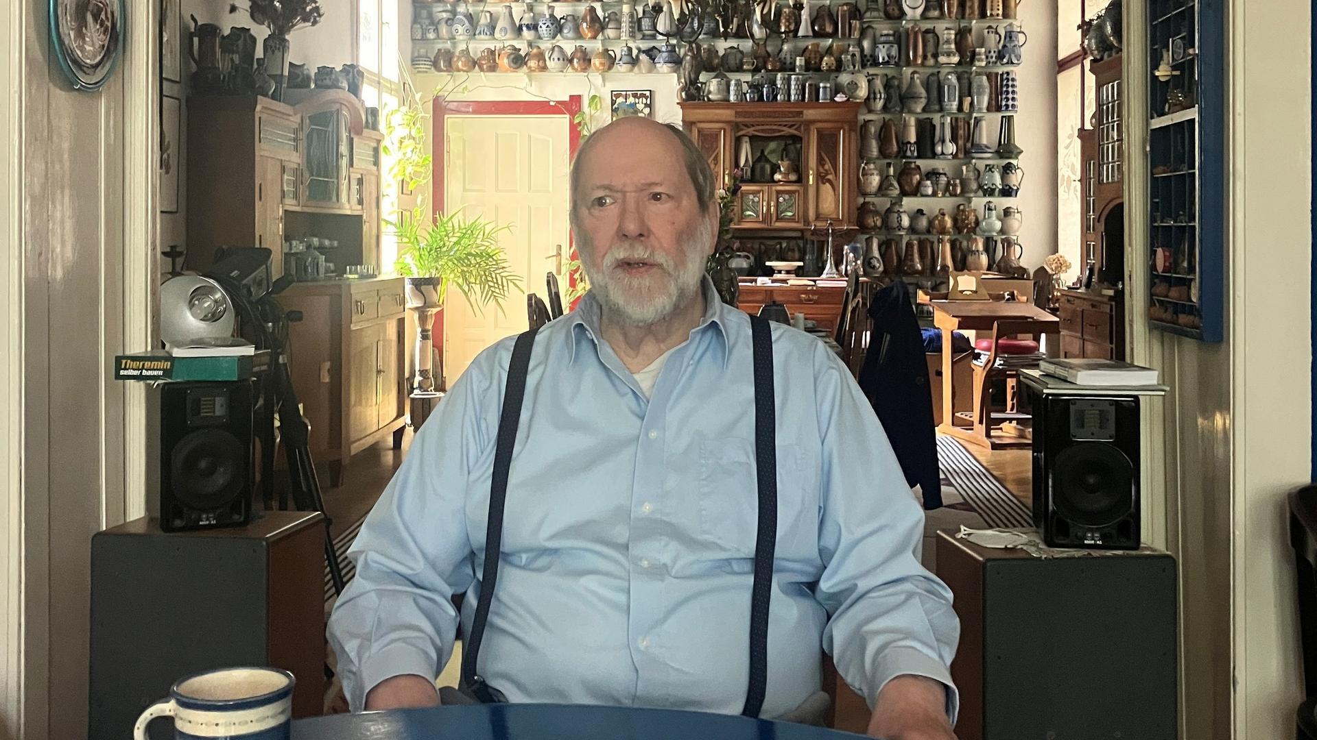 Ein Mann sitzt an einem Tisch, hinter ihm an der Wand ist eine Keramiksammlung sichtbar Ein Mann sitzt an einem Tisch, hinter ihm an der Wand ist eine Keramiksammlung sichtbar