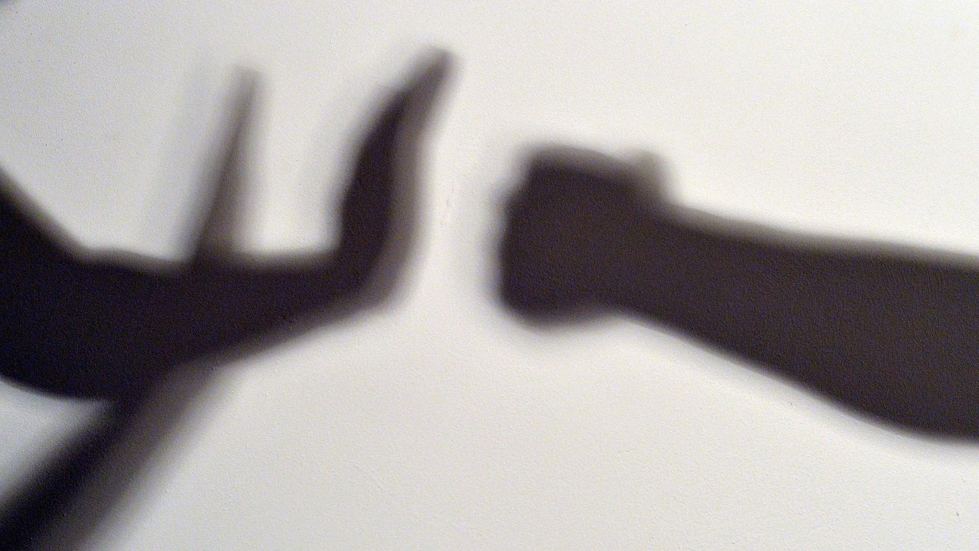 Gestelltes Bild zum Thema häusliche Gewalt - Schatten symbolisieren, wie eine Person sich vor der Gewalt einer anderen schützt.