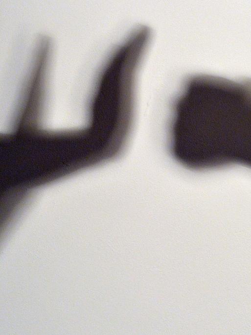 Gestelltes Bild zum Thema häusliche Gewalt - Schatten symbolisieren, wie eine Person sich vor der Gewalt einer anderen schützt.